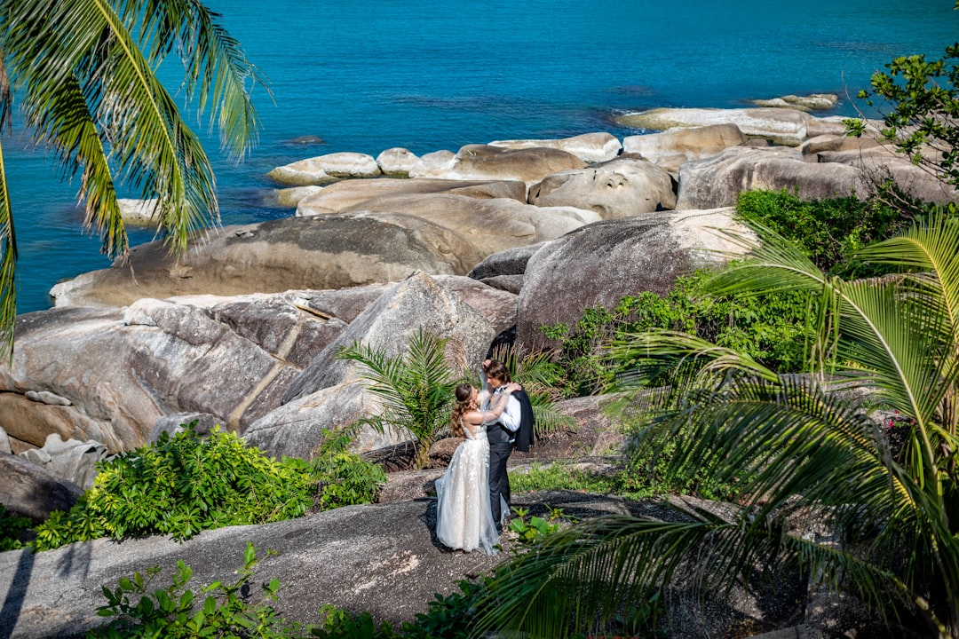A bride and groom standing on a rock by the ocean,