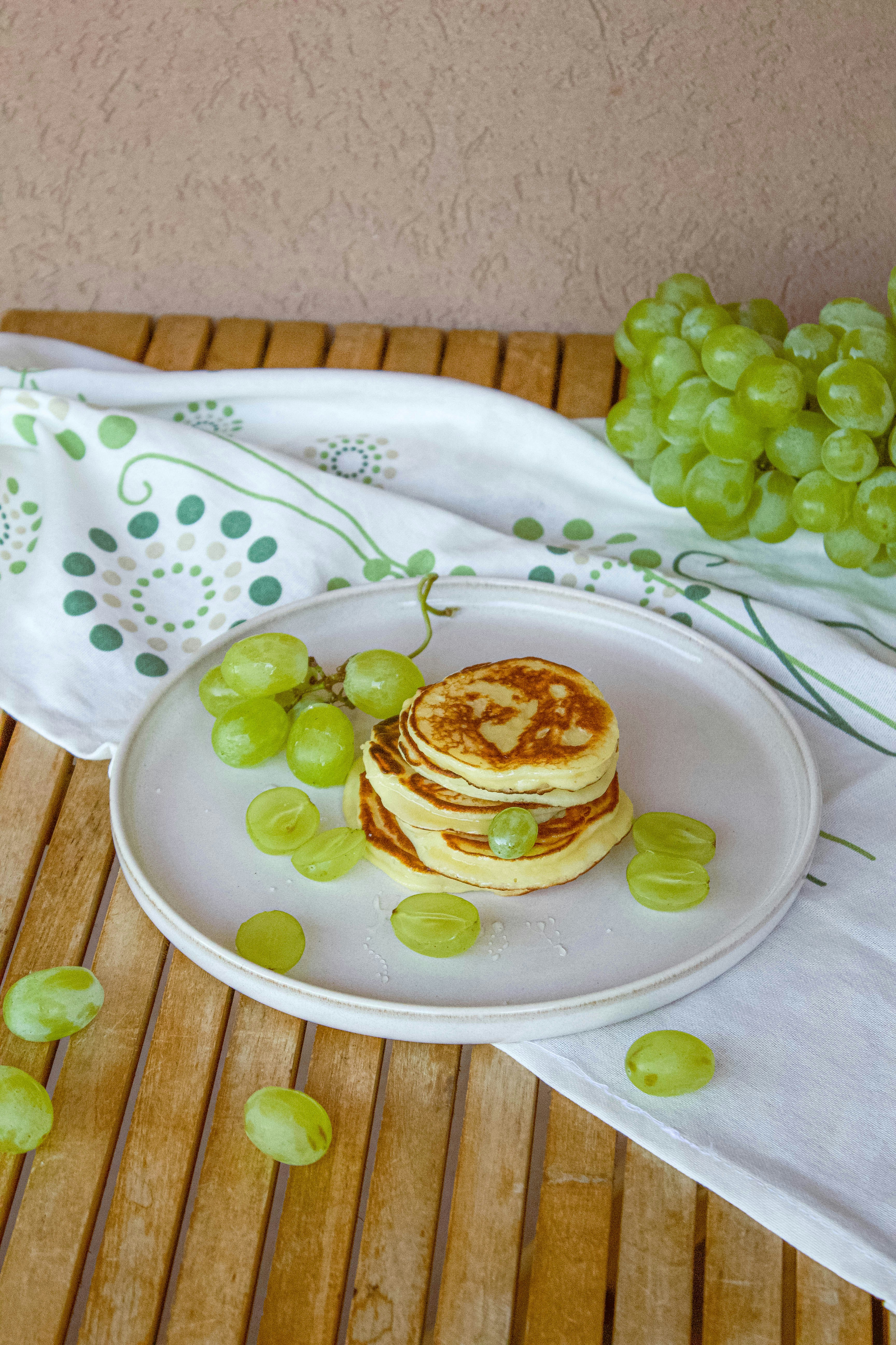 Ein weißer Teller mit einem Stapel Pfannkuchen neben grünen Trauben