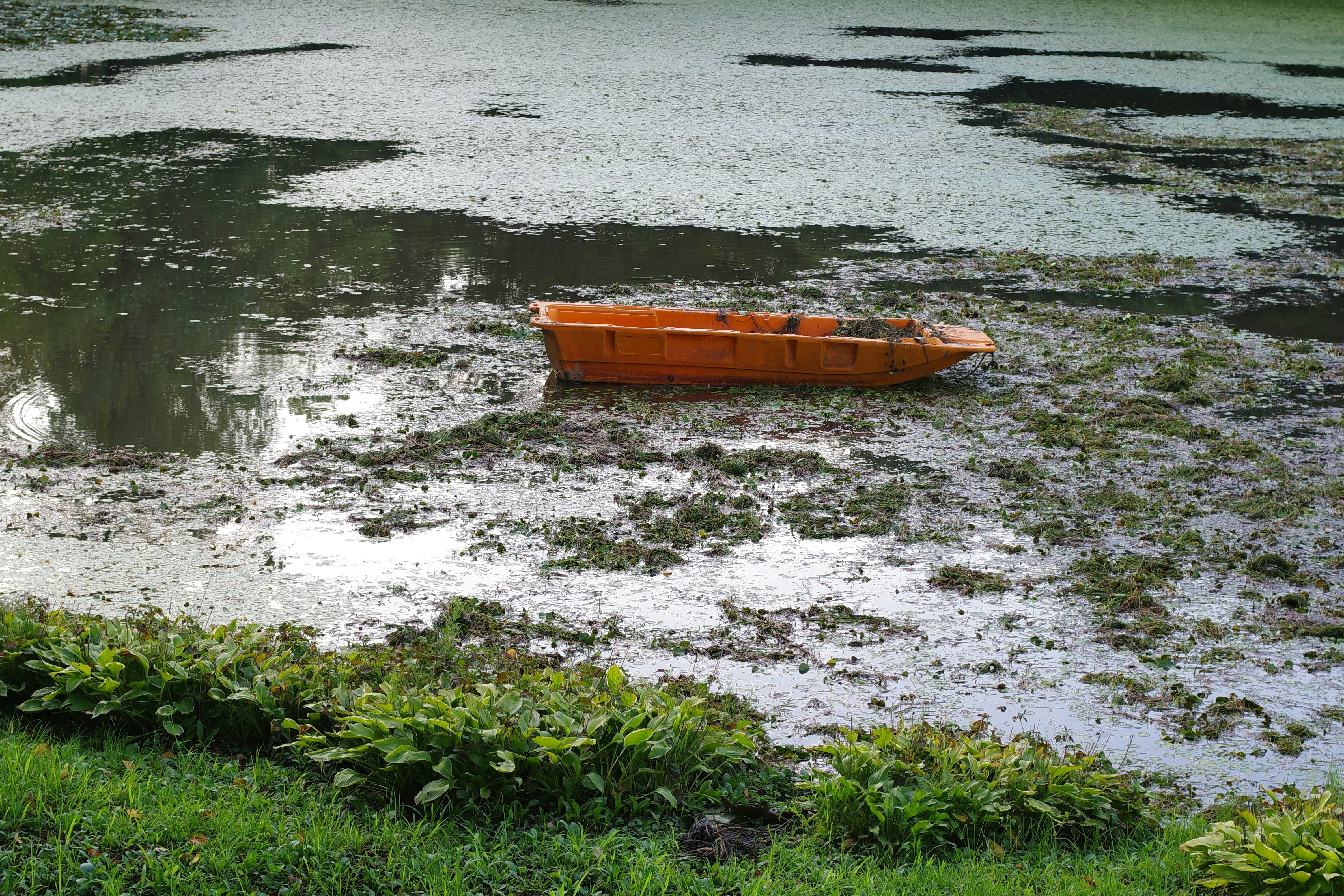 A small orange boat floating on top of a body of water