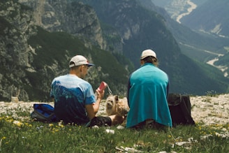 A couple of men sitting on top of a lush green hillside