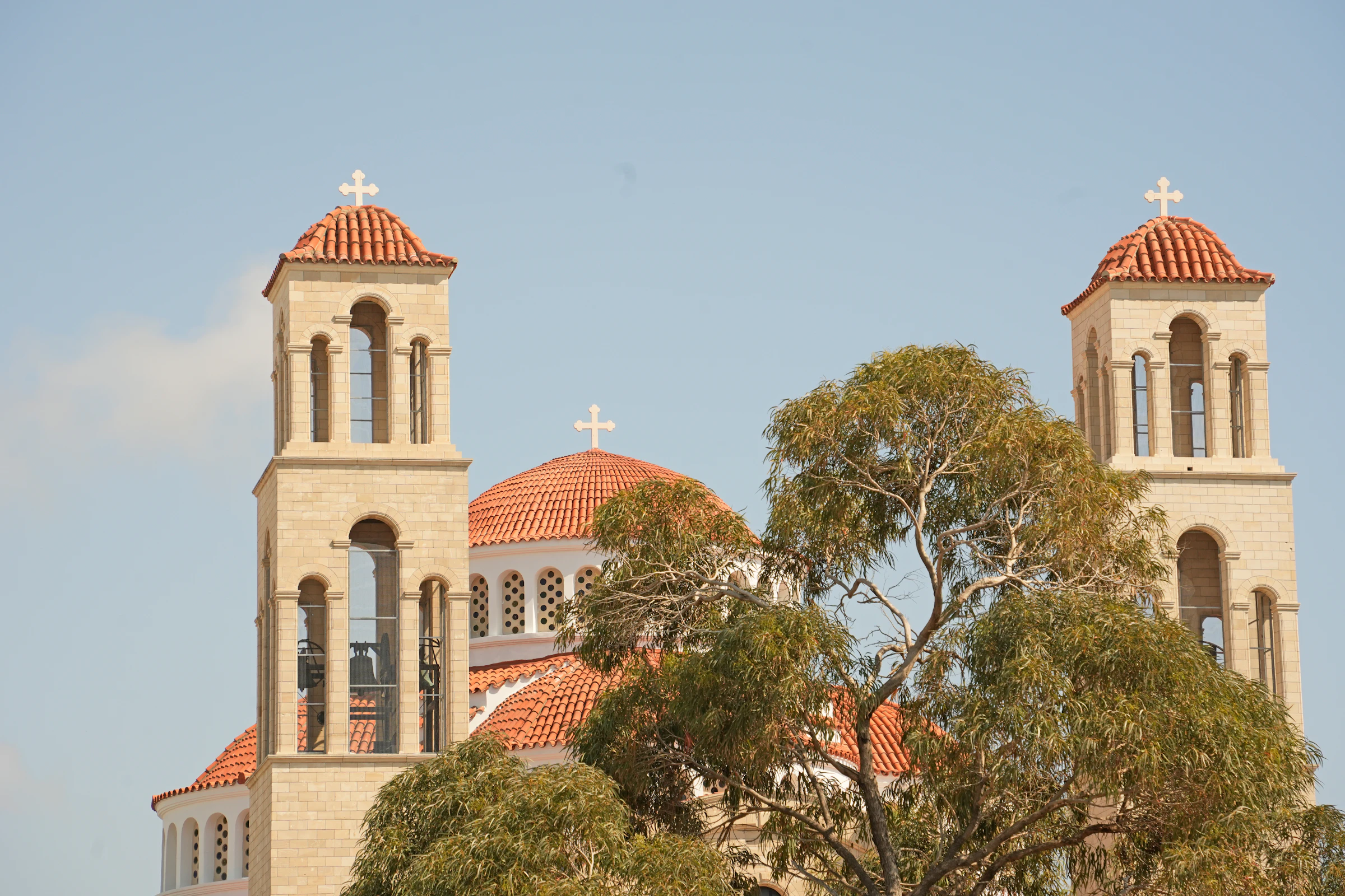 Twin stone bell towers and terracotta-tiled domes of a Greek Orthodox church in Cyprus against a pale blue sky