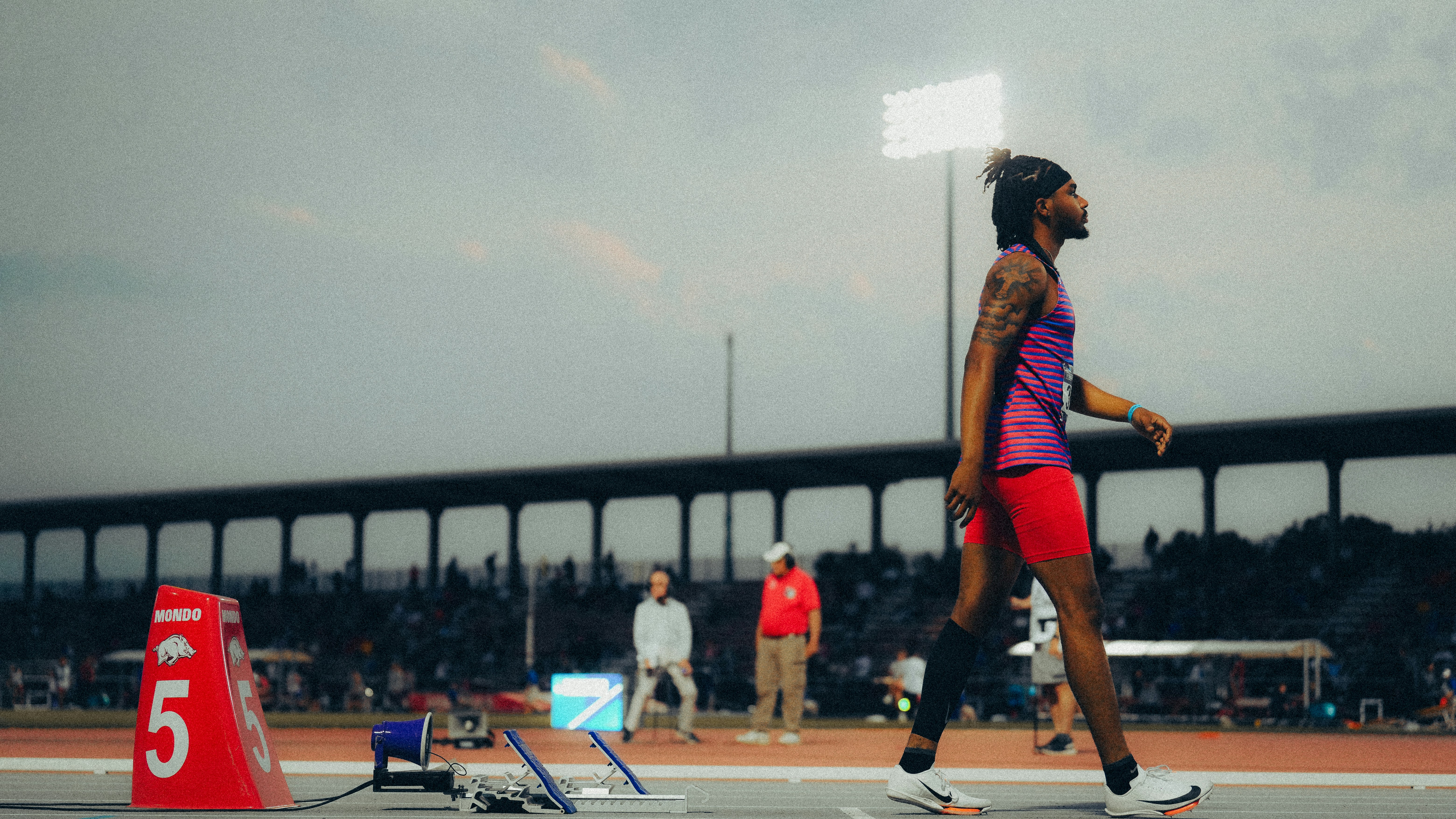 SoleStore athlete running on track in low-light stadium environment with dark shadows