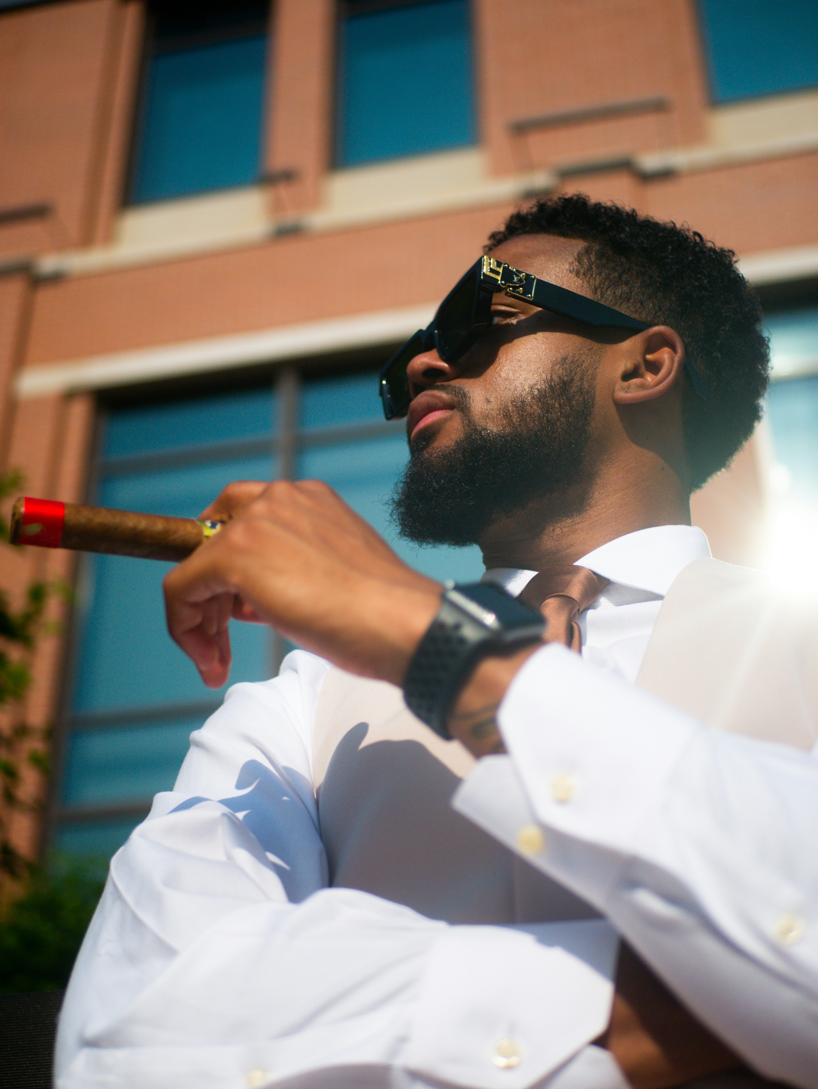 Un hombre con camisa blanca y gafas de sol sosteniendo un cigarro