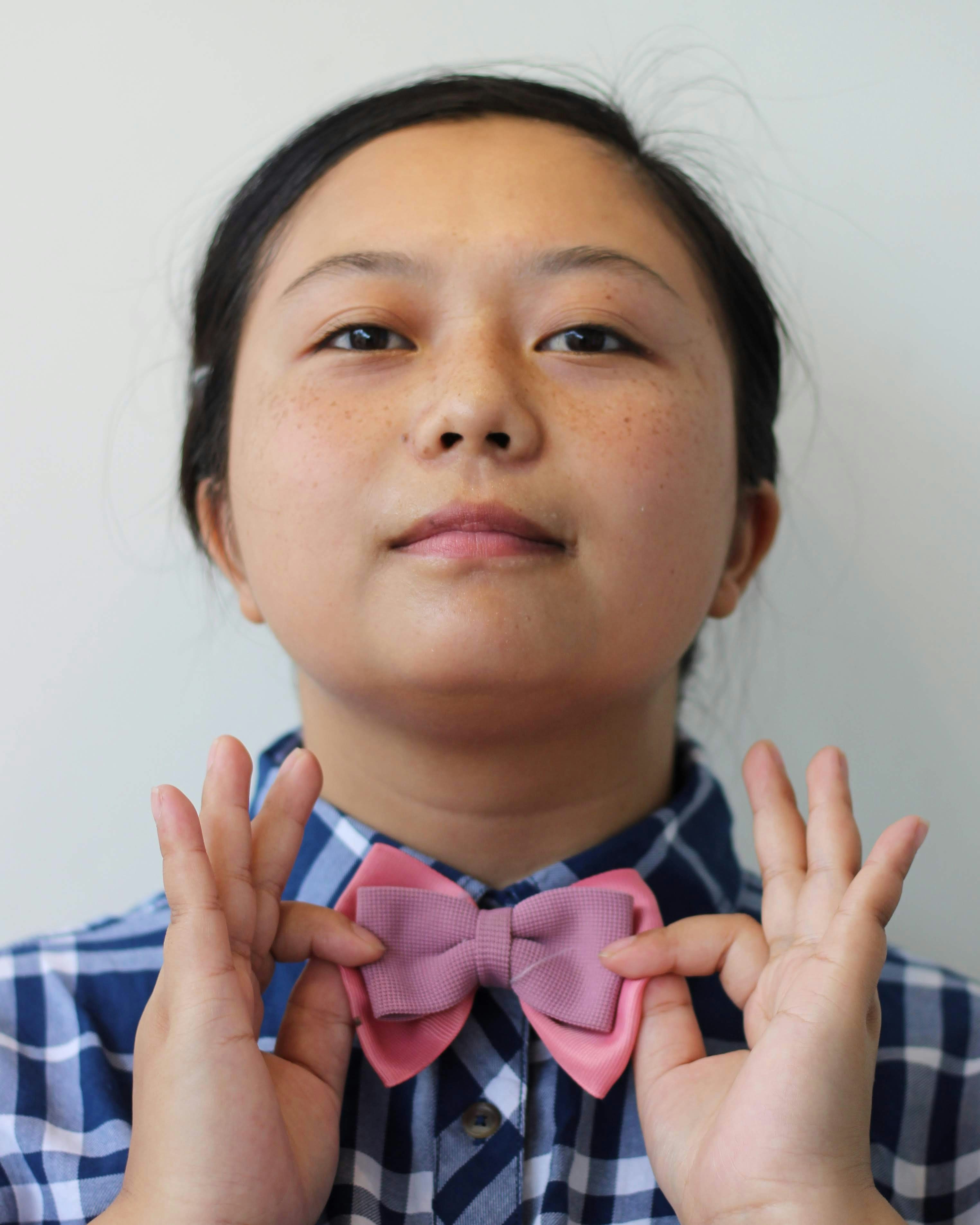 A young girl wearing a bow tie and holding her hands up