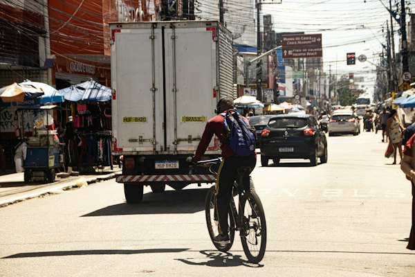 A man riding a bike down a street next to a truck — Fortaleza, Brazil