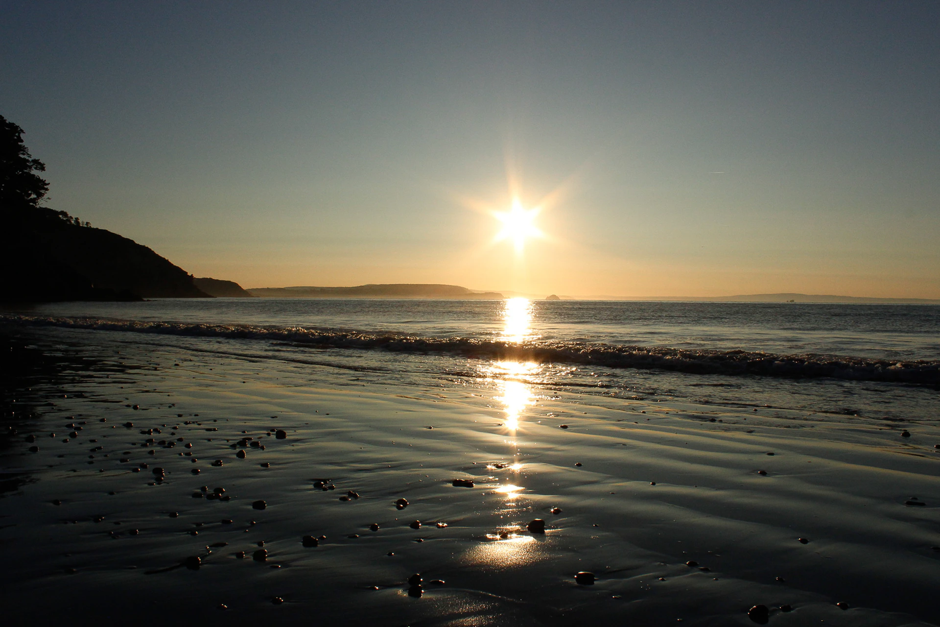 The sun is setting over the water at the beach
