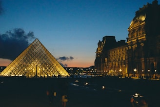 A large building with a very tall glass pyramid in front of it