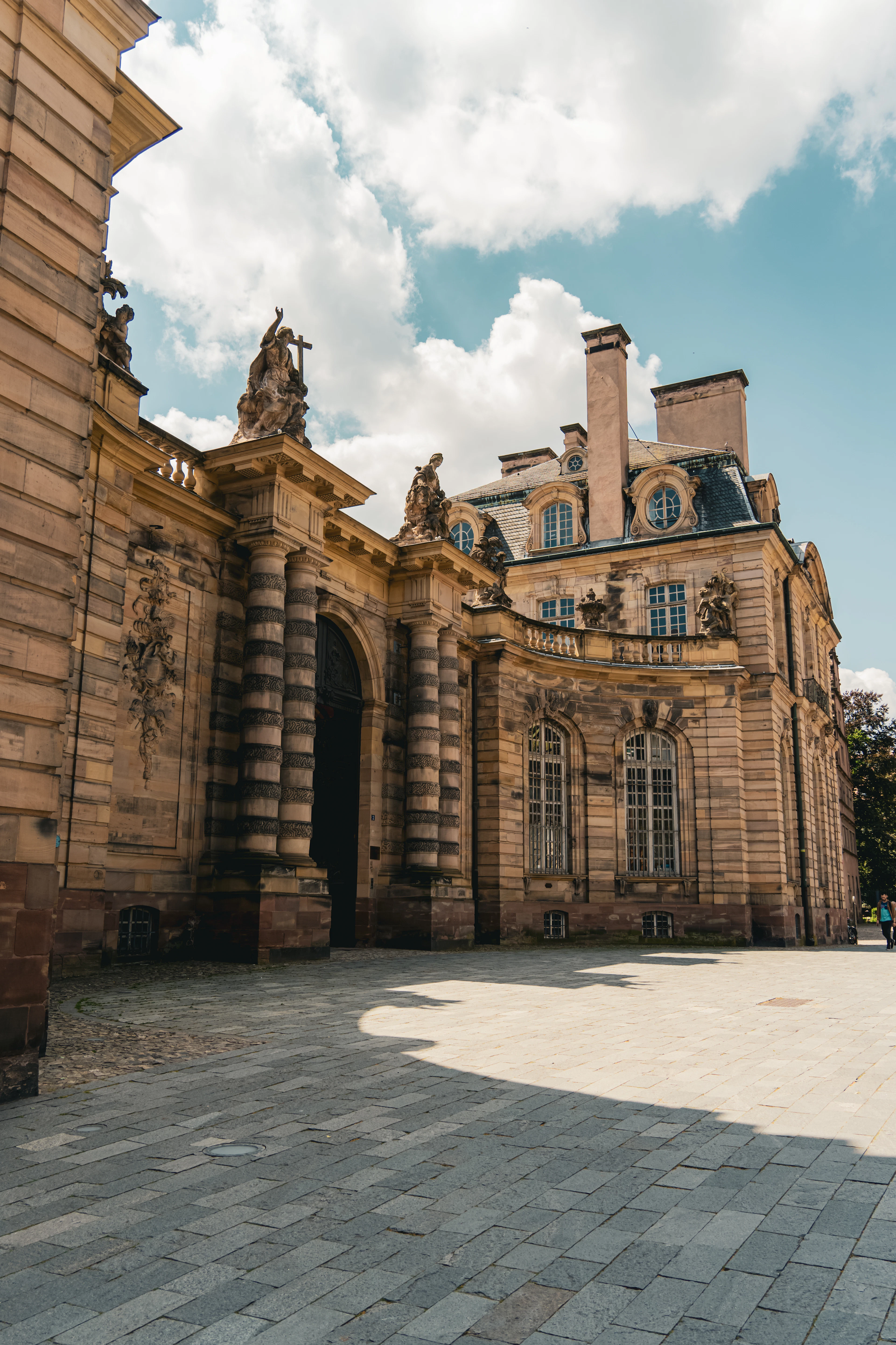 The ornate baroque stone facade of a grand Strasbourg palace, with statues and columned archways, under a partly cloudy sky.