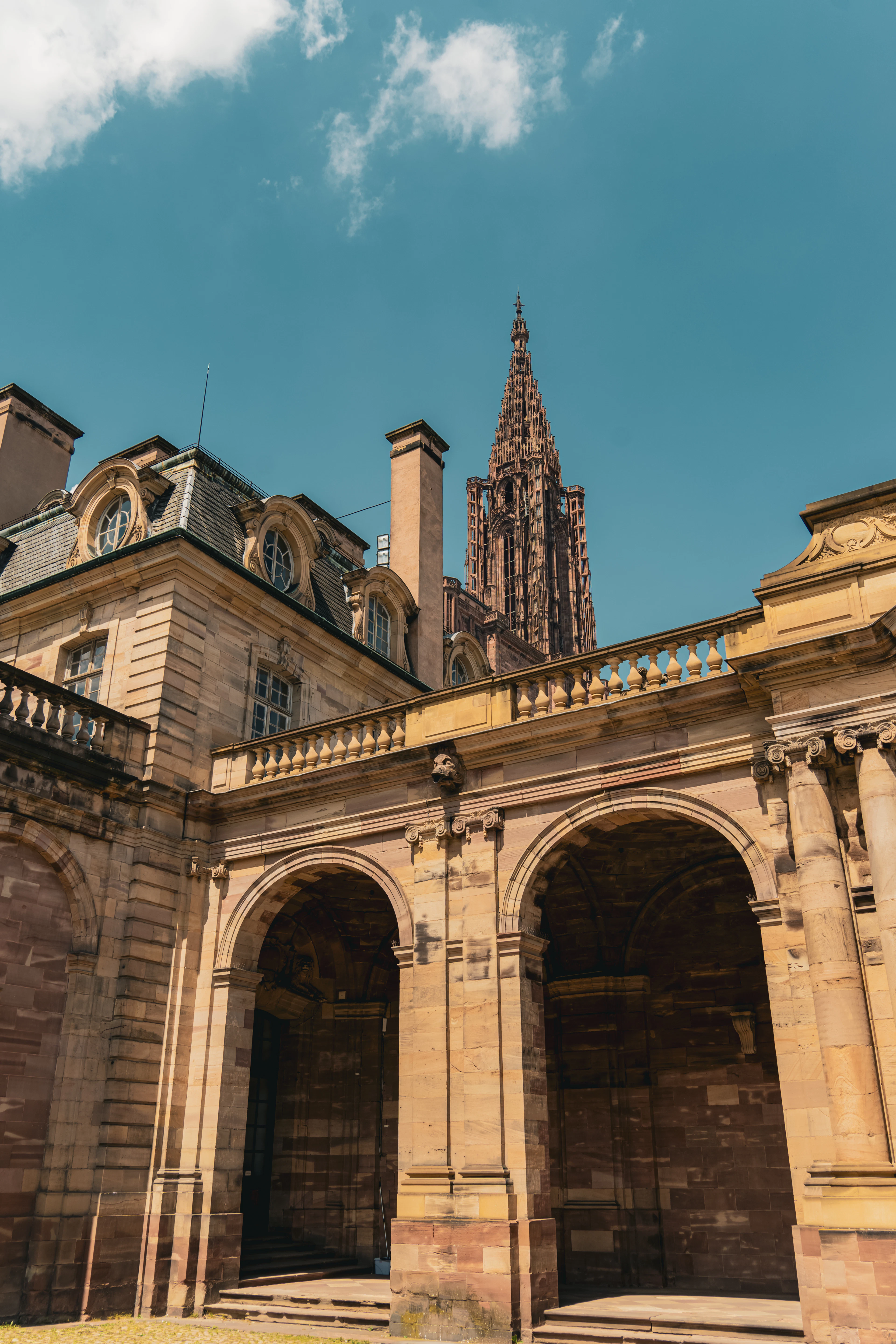 Strasbourg Cathedral's Gothic spire rises above a golden sandstone courtyard with stone arches.