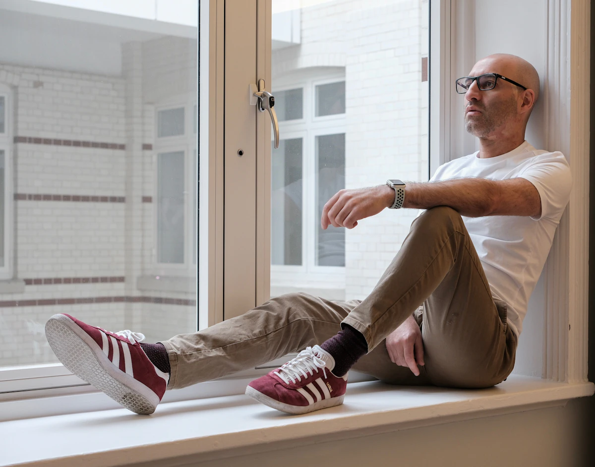 Person sitting on a windowsill looking out at the city — representing the possibility of a different relationship with anxiety and stress