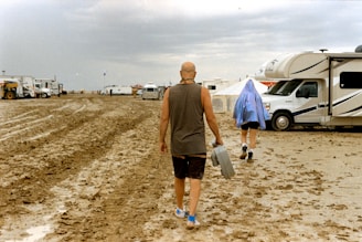 A man walking across a dirt field next to a camper