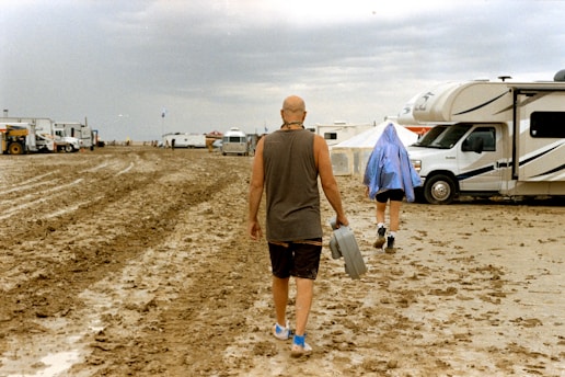A man walking across a dirt field next to a camper