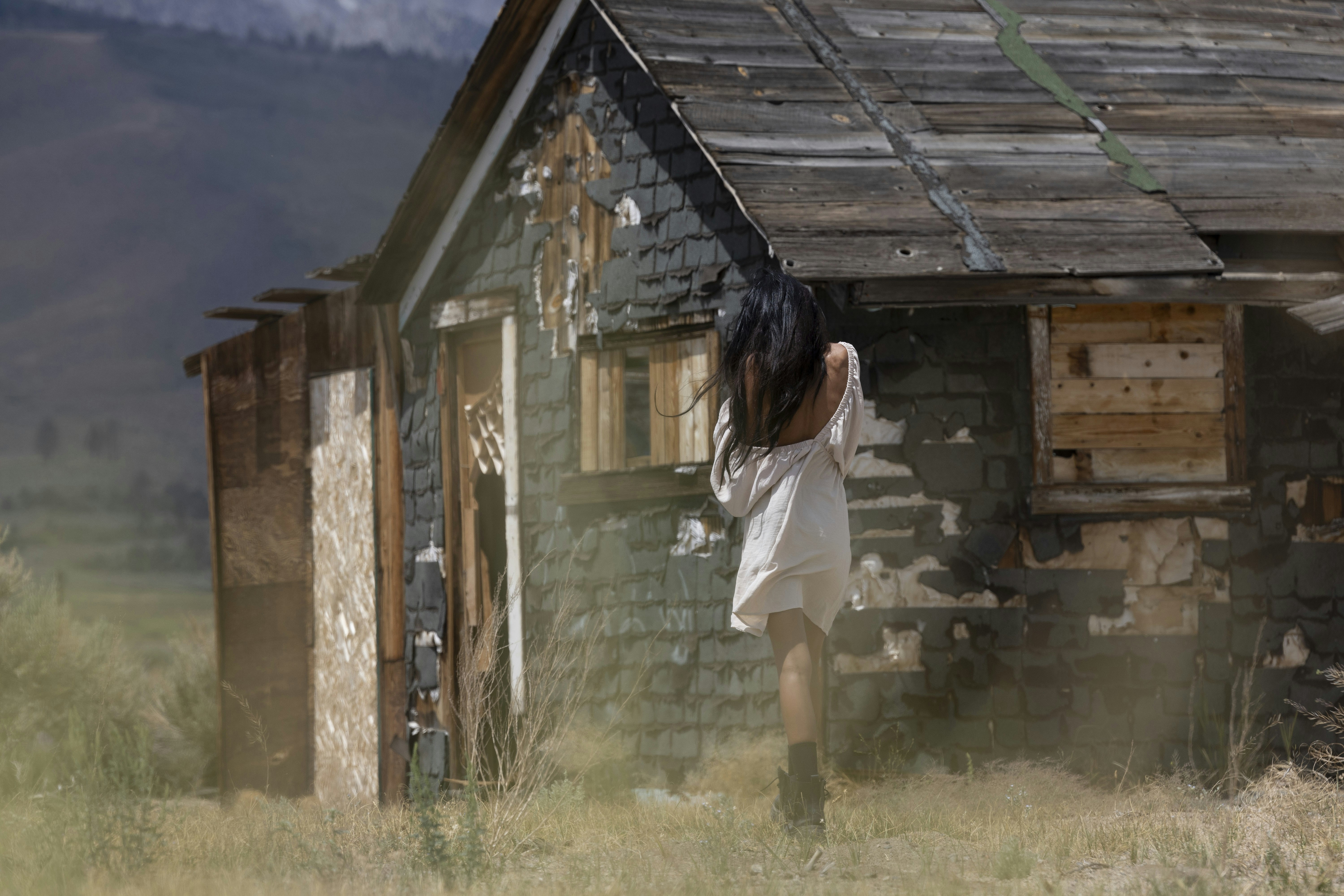 Woman in white dress in front of shack