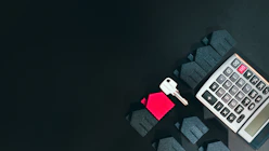 A silver key, a red house model, and a calculator on a black surface