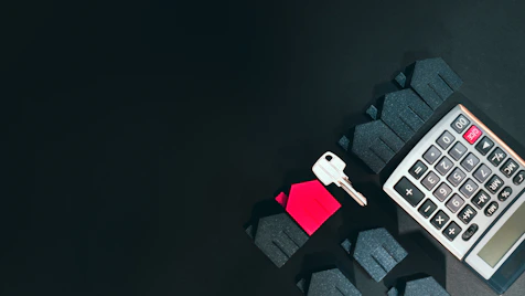 A silver key, a red house model, and a calculator on a black surface