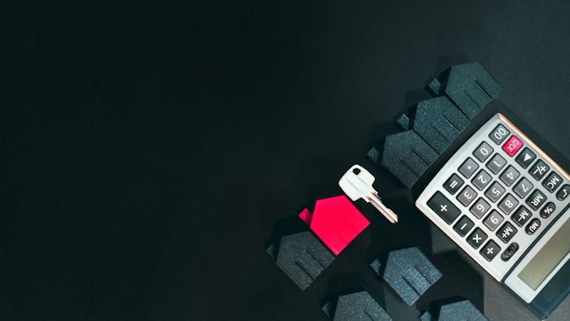 A silver house key, a small red model house, and a calculator on a dark table, representing the math of a Las Vegas mortgage payment at a 7 percent rate