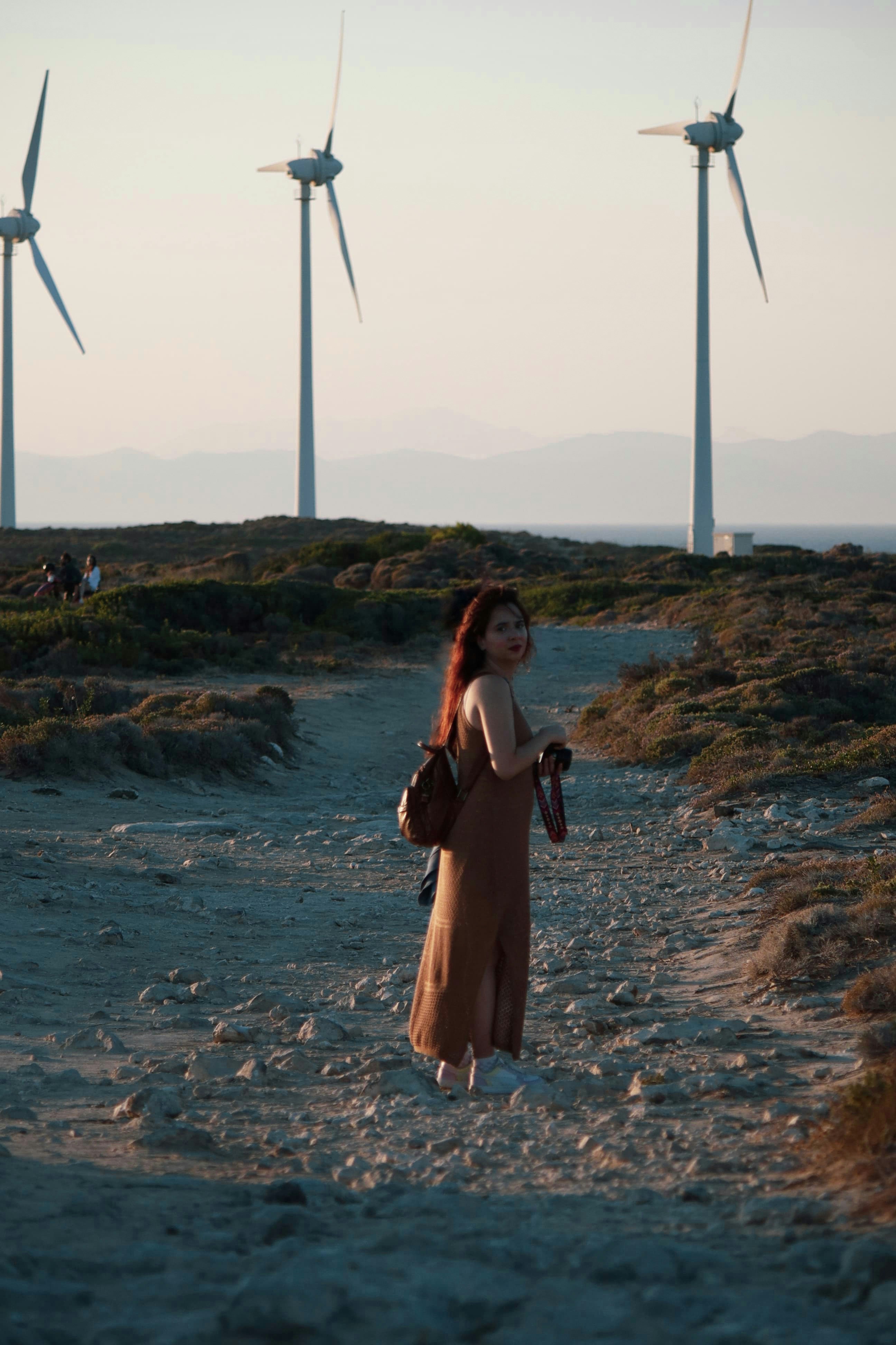 A woman walking down a dirt road next to wind turbines