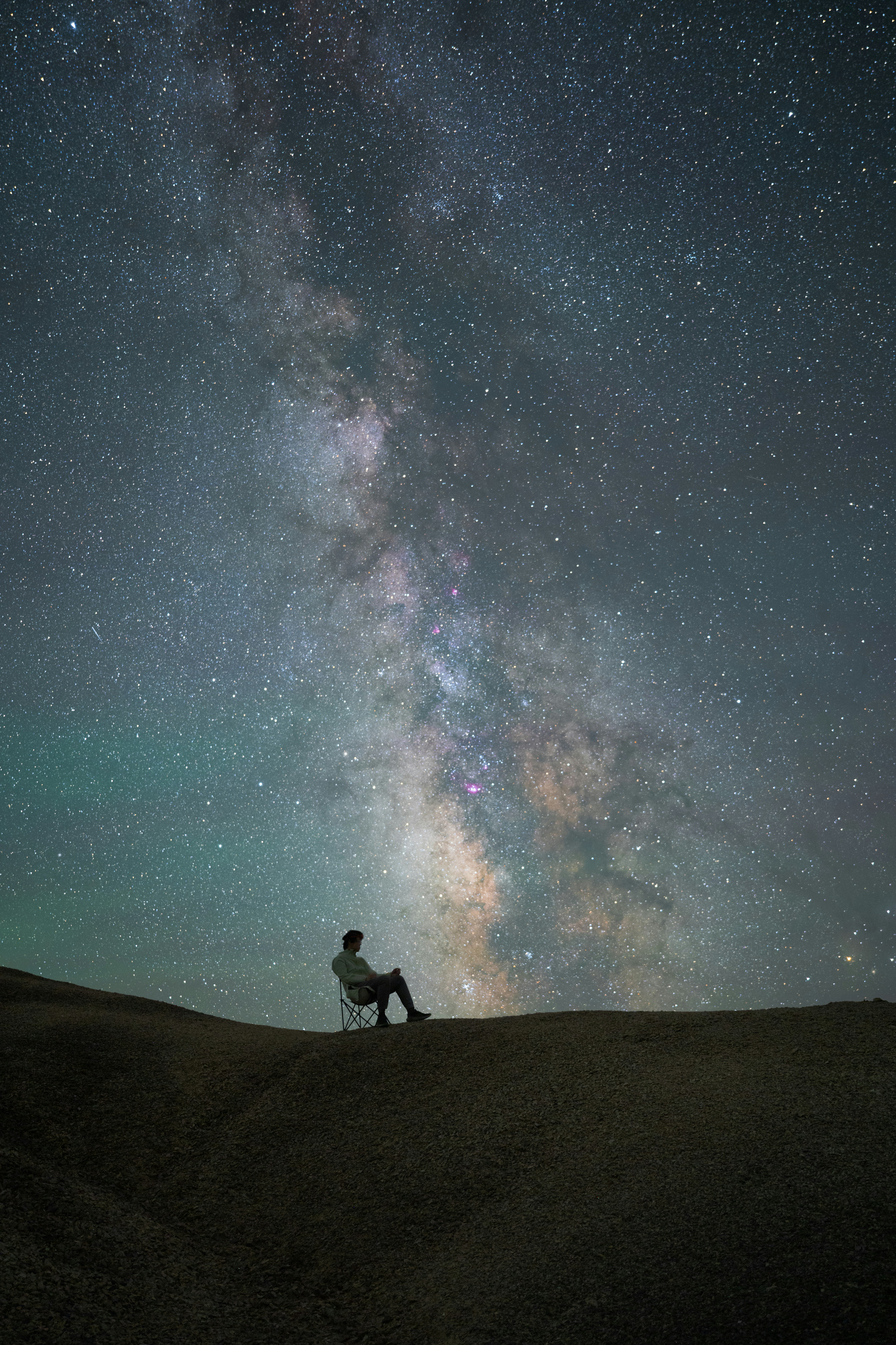A man sitting on top of a hill under a night sky filled with stars