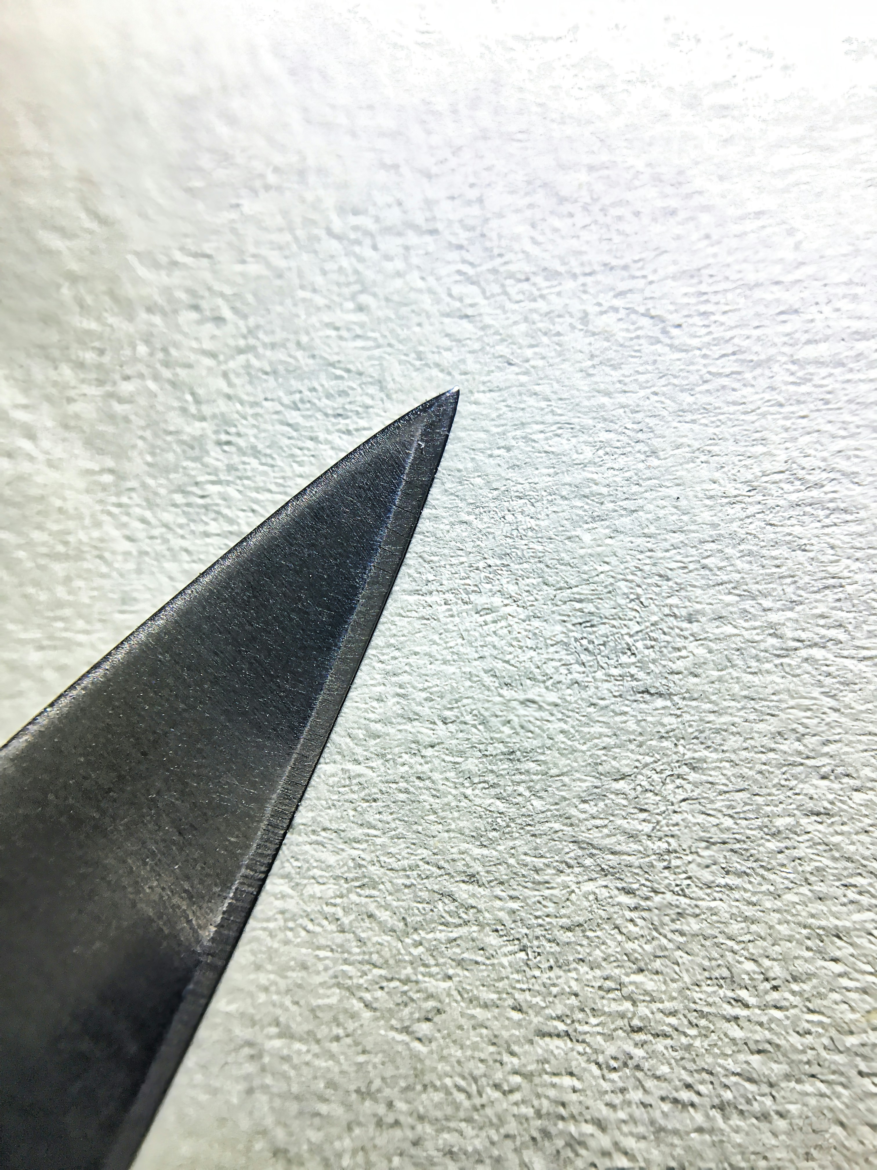 Sharp knife blade close-up on dark wooden surface, dramatic side lighting, deep moody shadows, dark kitchen atmosphere
