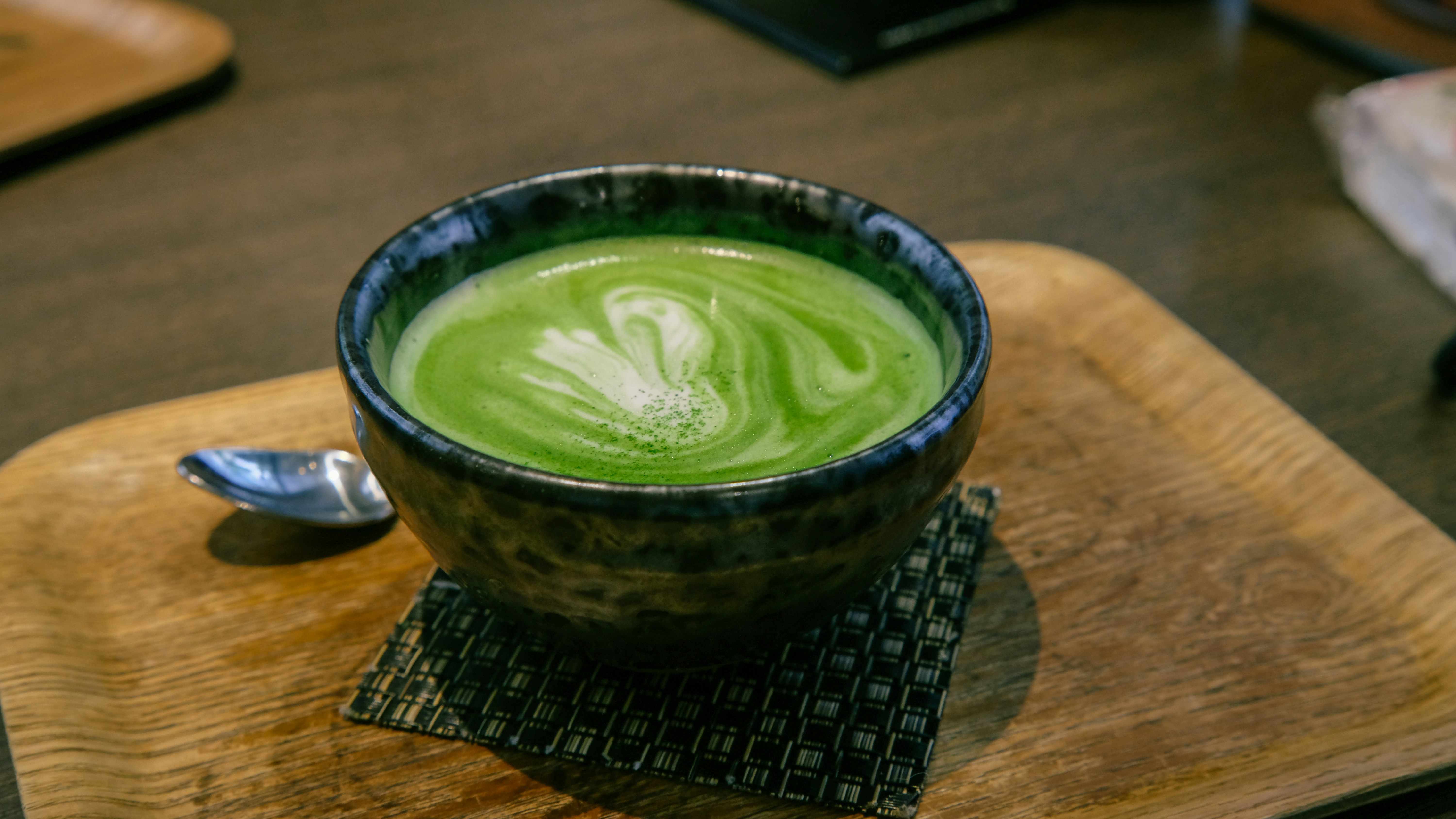 Vibrant green matcha latte in a ceramic cup with foam art on a wooden tray