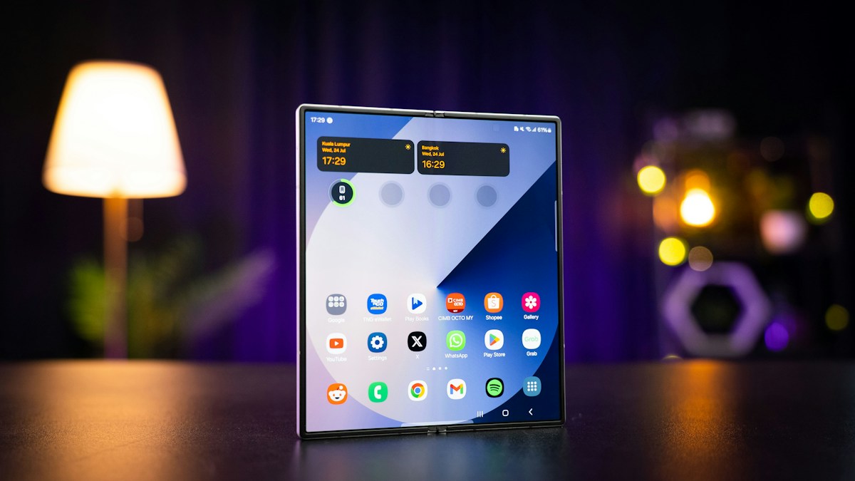 Smartphone pliable ouvert, écran d'accueil allumé, posé sur une table devant une lampe, en illustration