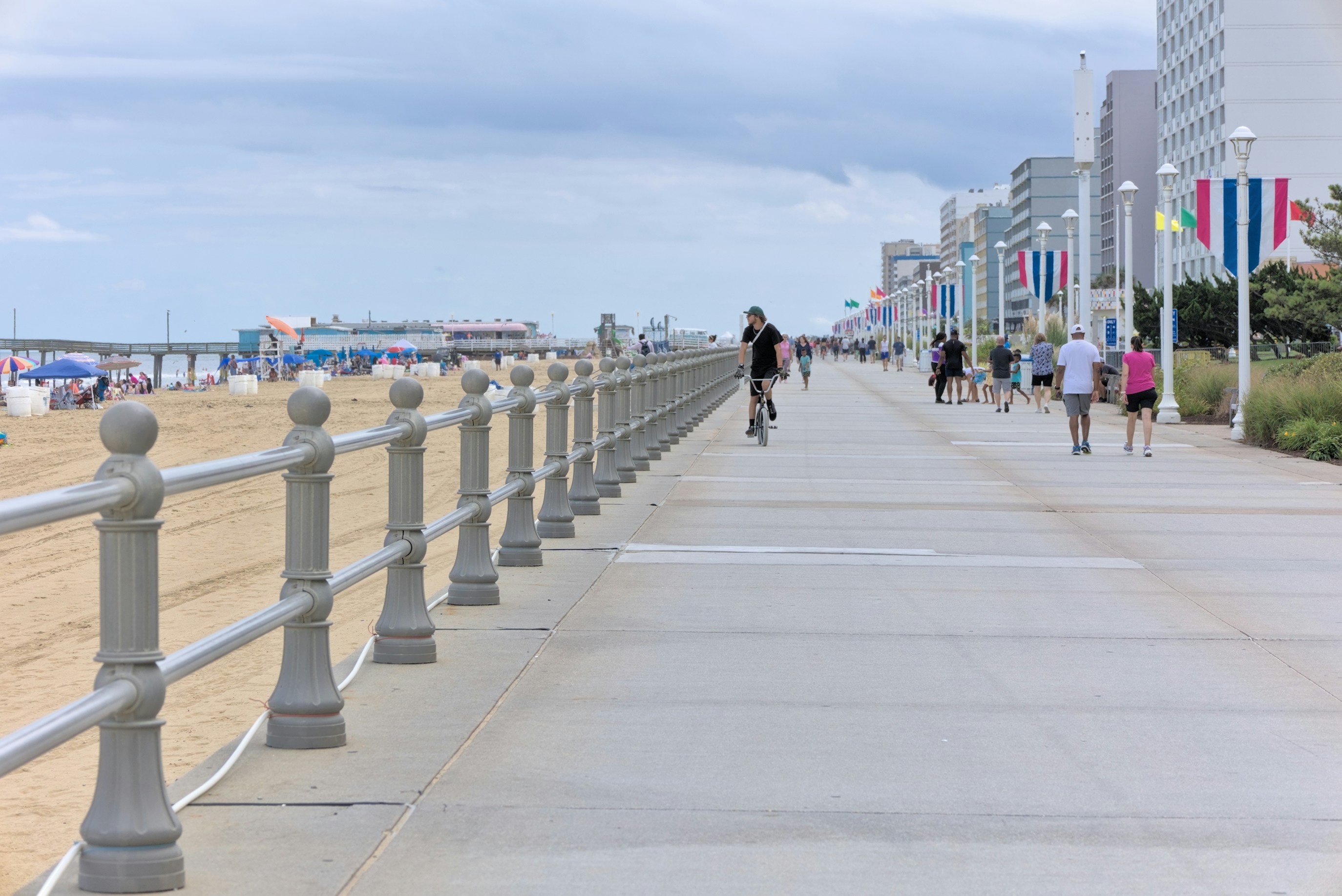 A group of people walking down a sidewalk next to a beach