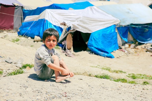 A young boy sitting on the ground in front of tents