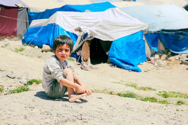 A young boy sitting on the ground in front of tents
