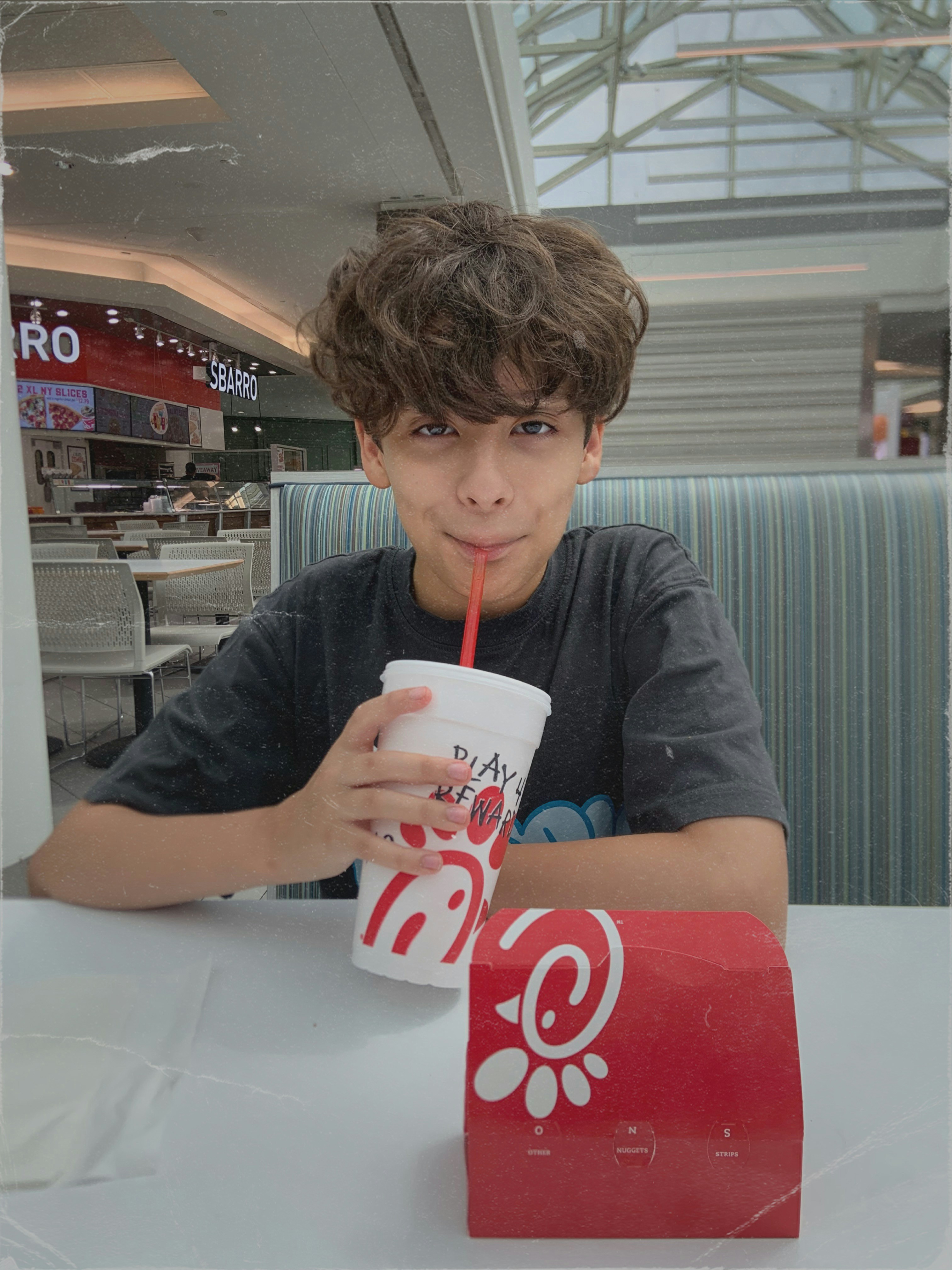 A young boy sitting at a table with a drink in his hand
