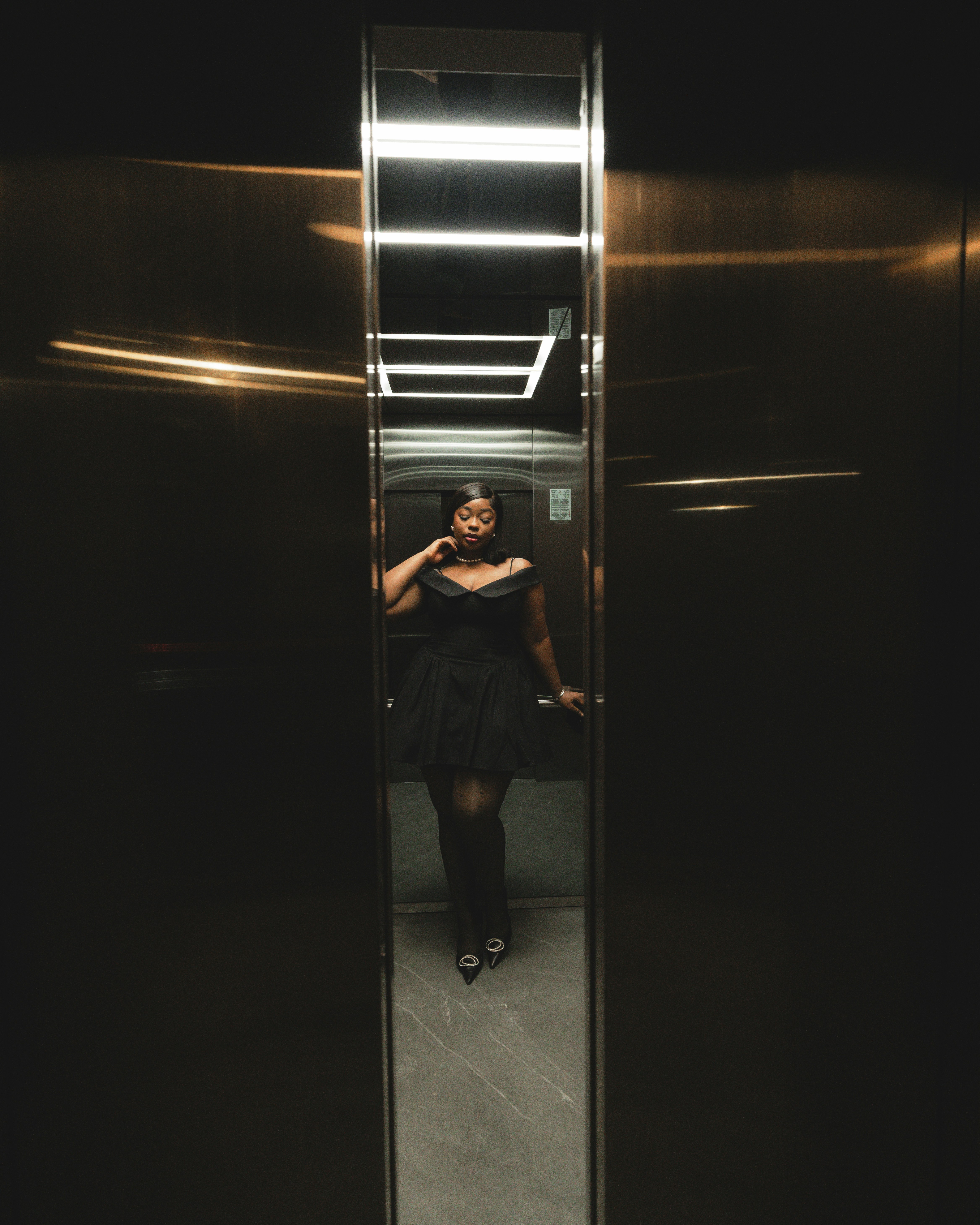 A woman in a black dress standing in a elevator