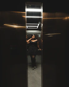 A woman in a black dress standing in a elevator