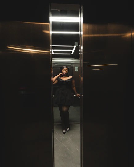 A woman in a black dress standing in a elevator
