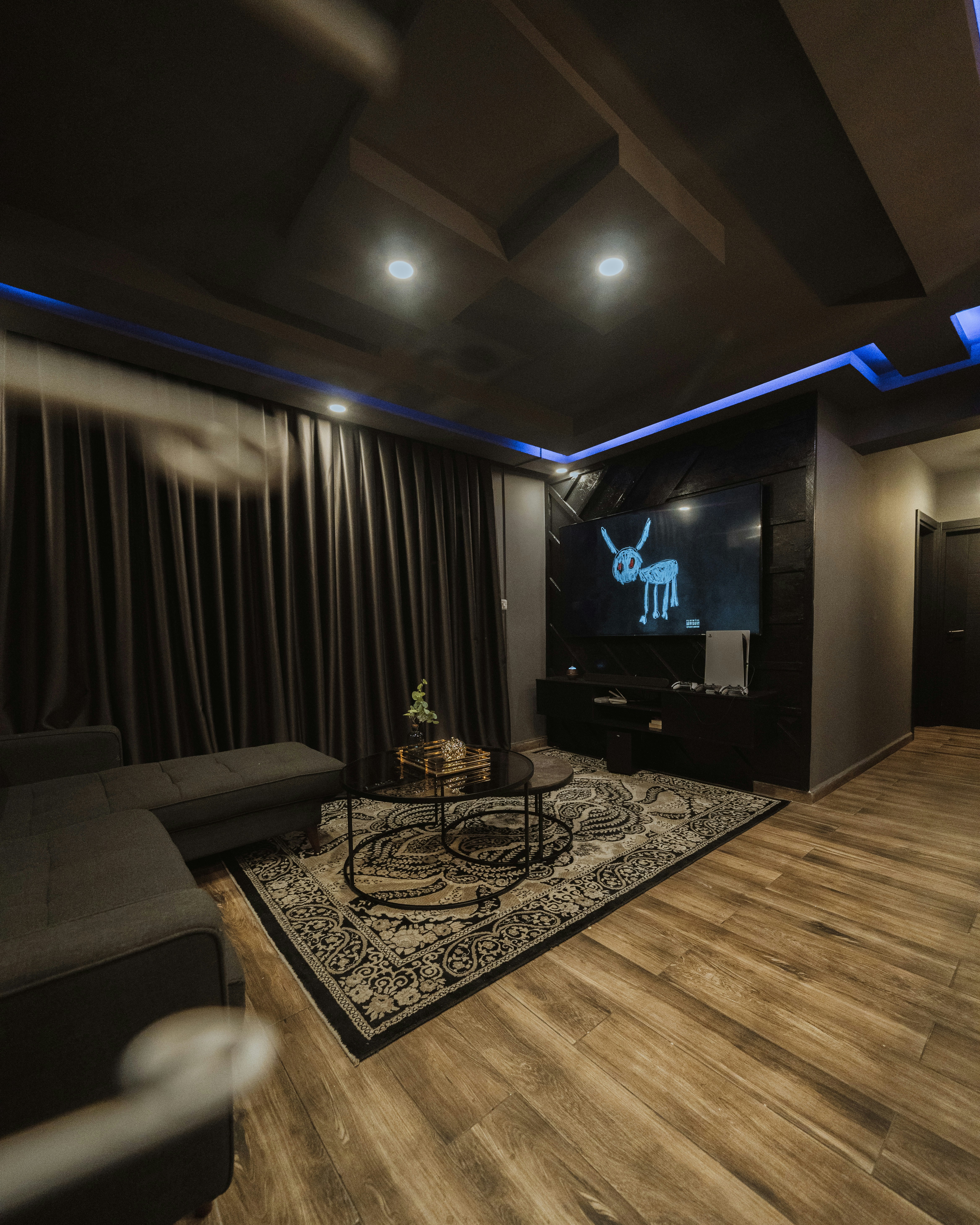 Sleek dark living room with vibrant blue cyan LED lighting behind large TV, modern sofa, atmospheric low-key lighting