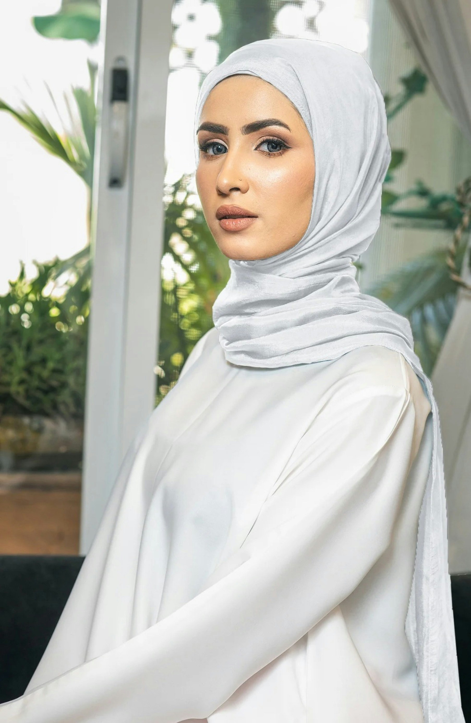 A woman in a white hijab standing in front of a window