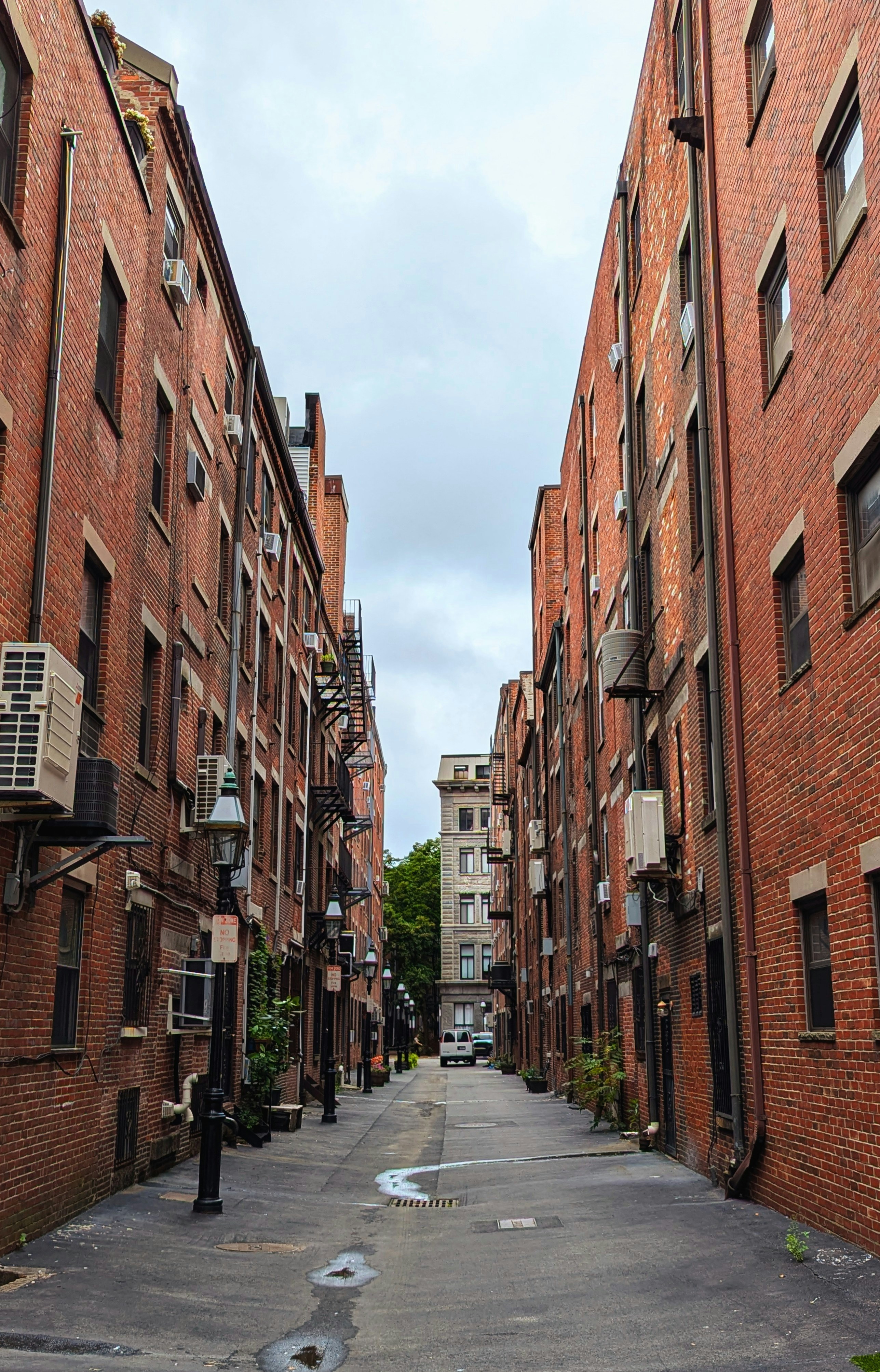 A narrow alley with brick buildings and air conditioners