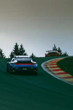 Two cars driving on a race track with trees in the background