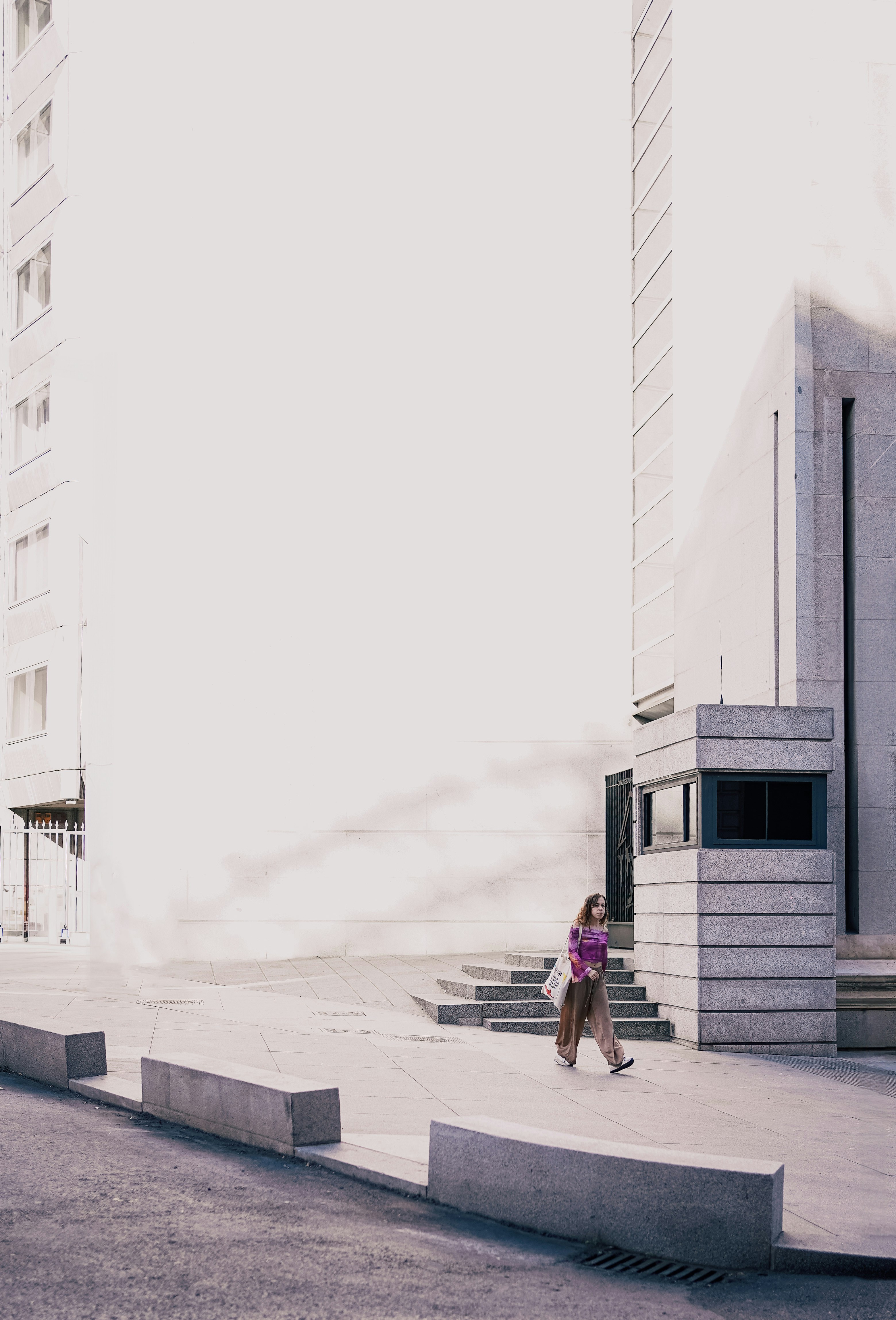 고층 건물 옆 거리를 걷고 있는 한 여성