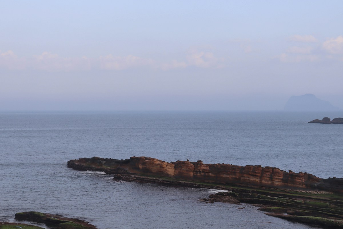 野柳海岬旁層層岩層延伸入海，遠方海面上是基隆嶼