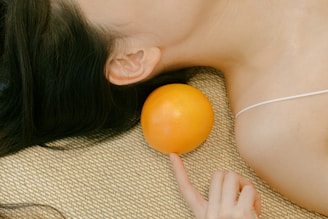 A woman laying on the floor with an orange in her hand