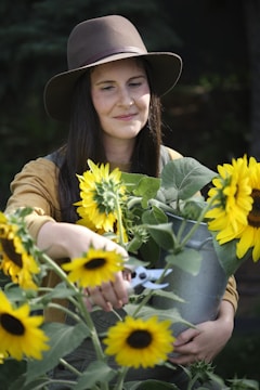 A woman in a hat holding a bucket of sunflowers