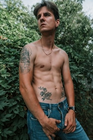 A shirtless man standing in front of a bush