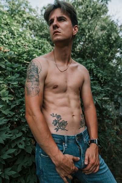 A shirtless man standing in front of a bush