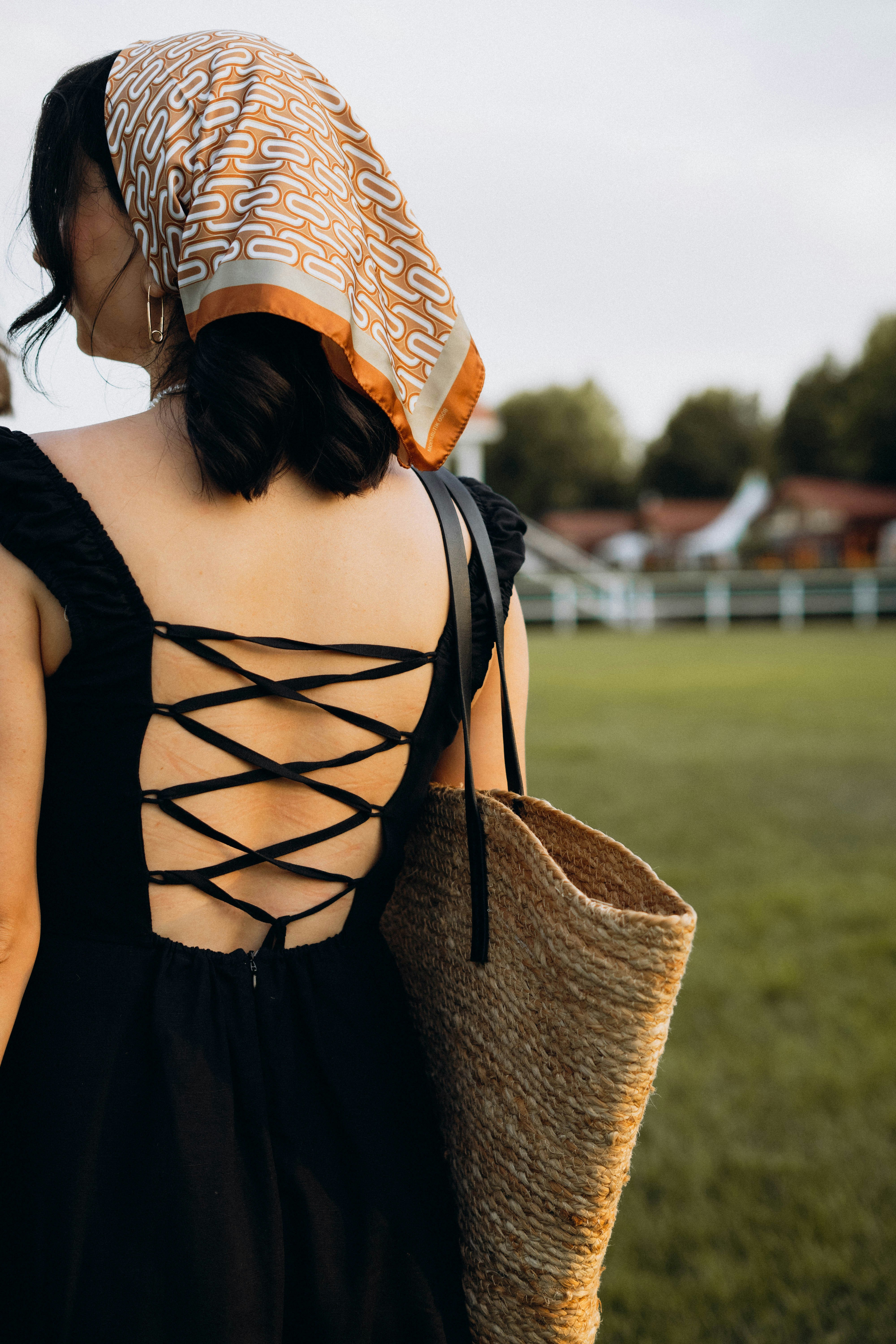 A woman in a black dress is holding a straw bag
