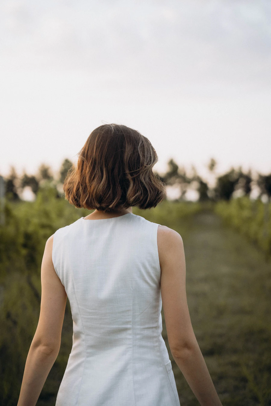 An adult walking through a green field at golden hour, seen from behind in soft warm light, a calm steady hopeful moment