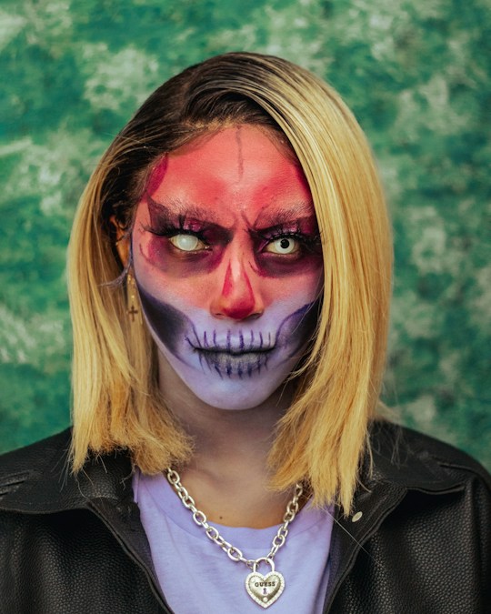 Un visage maquillé pour Halloween, front rouge, yeux blancs et mâchoire de squelette dessinée sur fond pâle