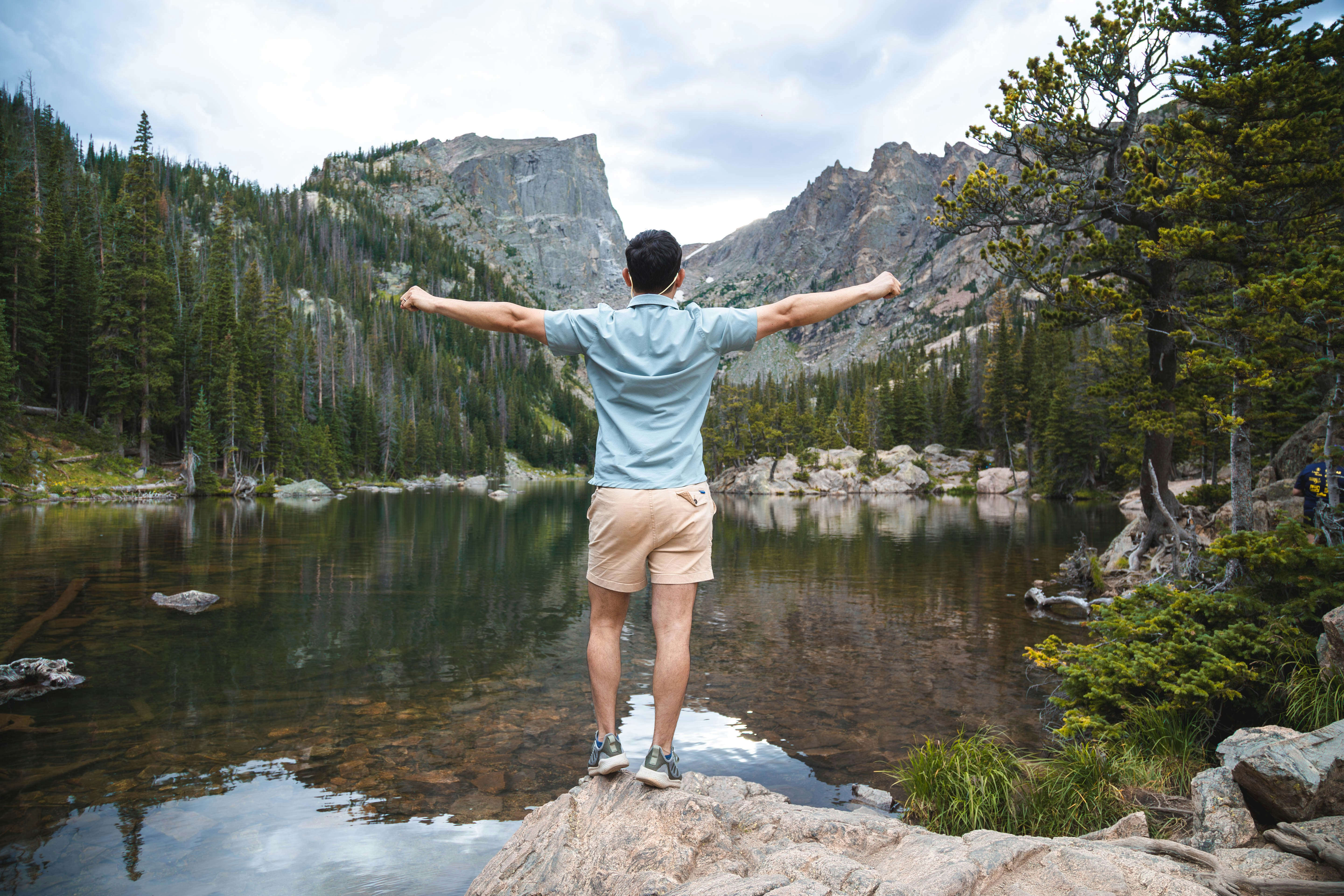 A man standing on top of a rock next to a lake