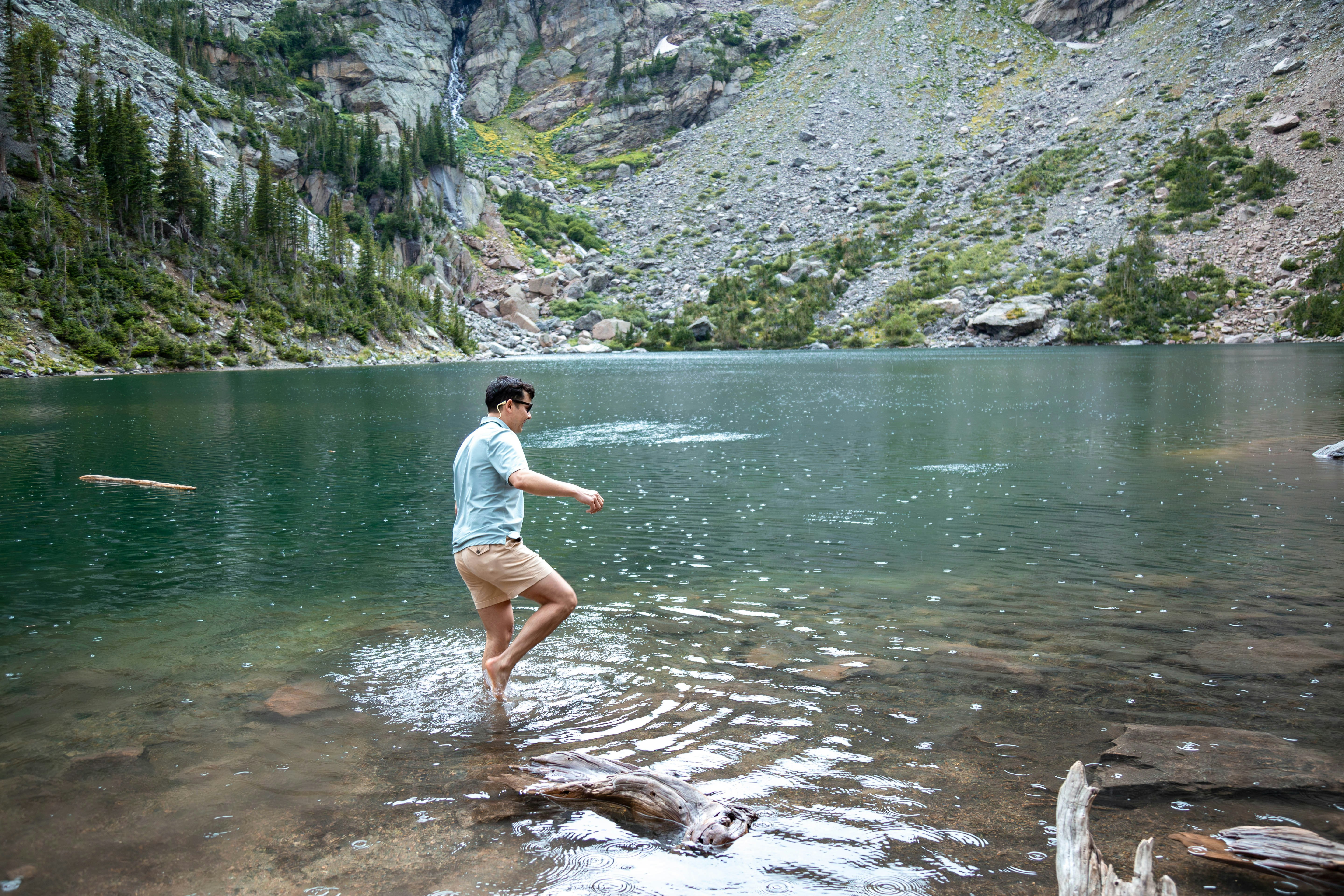 A man is wading in the water near a mountain