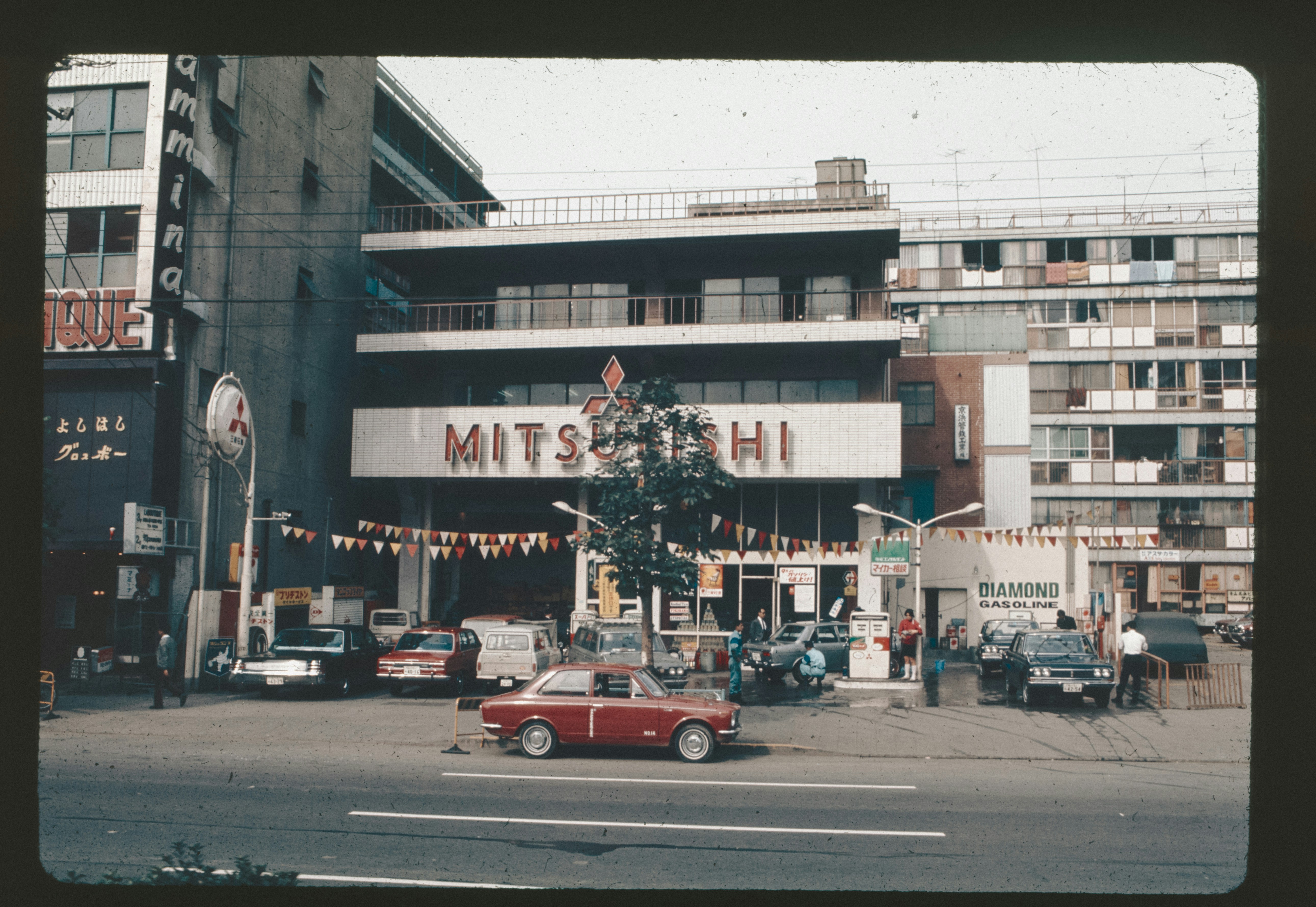 A red car driving down a street next to tall buildings