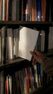 A person holding a book in front of a bookshelf