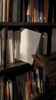 A person holding a book in front of a bookshelf